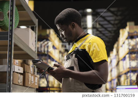 Black e-commerce employee scanning awb tracking numbers, registering shipping labels and details for the warehouse inventory records. Handling pallets import export operations. 131700159