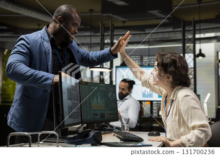 Happy colleagues sharing a high five after successful tasks accomplishment, enjoying triumph and feeling pleased with their expertise. Diverse people celebrating achievement, friendly space. 131700236