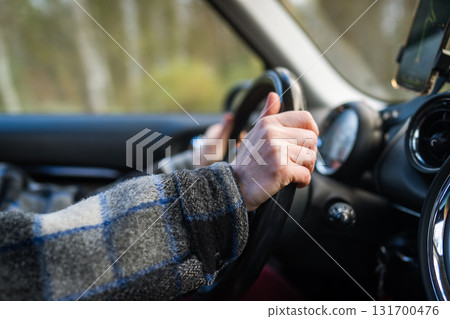 Closeup of woman hands holding steering wheel driving car, using navigation app on smartphone. 131700476