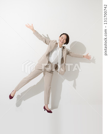 Full-body front view of a woman in a suit jumping with her arms outstretched in joy 131700742