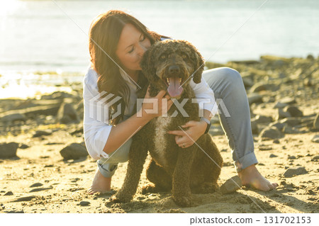 Portrait of one brown portuguese water dog outdoors on the beach with 40s woman 131702153