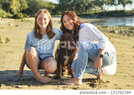 brown portuguese water dog outdoors on the beach with mother and daughter 131702194