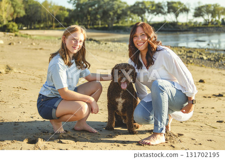 brown portuguese water dog outdoors on the beach with mother and daughter 131702195