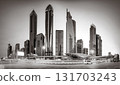 Monochrome city skyline with tall skyscrapers reflecting on calm water under a cloudy sky, Dubai Marina bay UAE 131703243