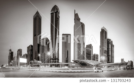 Monochrome city skyline with tall skyscrapers reflecting on calm water under a cloudy sky, Dubai Marina bay UAE 131703243