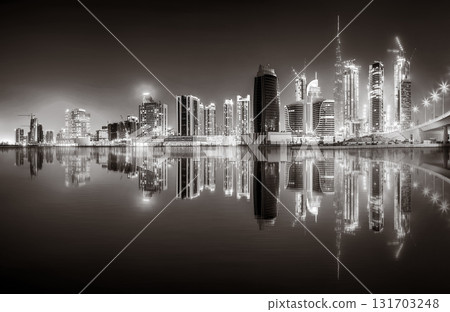 Urban city skyline with illuminated skyscrapers and waterfront railing in black and white at night, Dubai Marina bay UAE 131703248