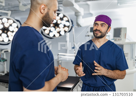 Two surgeons are seen in an operating room, engaged in a discussion, likely planning or reviewing a procedure. Two surgeons are seen in an operating room, engaged in a discussion, likely planning or reviewing a procedure. 131703510