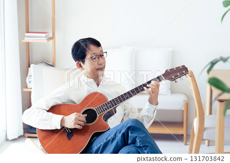Middle-aged man playing guitar in the living room Middle-aged man playing guitar in the living room 131703842