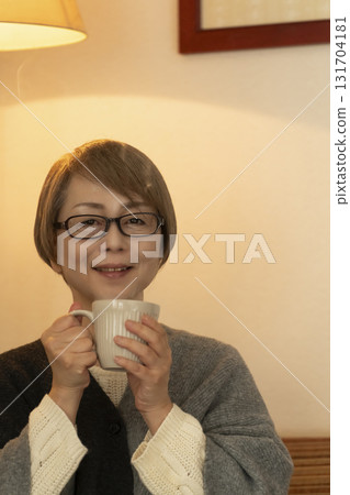 一位老年婦女在客廳喝著熱氣騰騰的飲料 一位老年婦女在客廳喝著熱氣騰騰的飲料 131704181