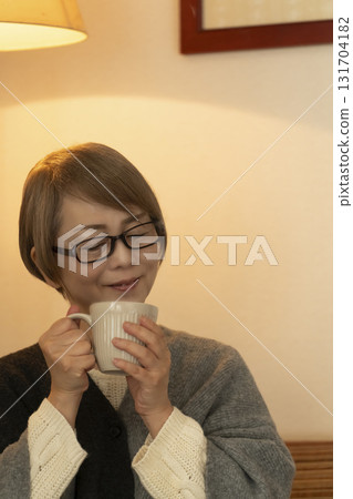 Senior woman drinking a steaming hot drink in the living room Senior woman drinking a steaming hot drink in the living room 131704182