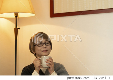 Senior woman drinking a steaming hot drink in the living room 131704194