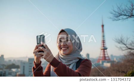Young Woman Smiling Taking Selfie with Smartphone in Front of Cityscape and Tower 131704372