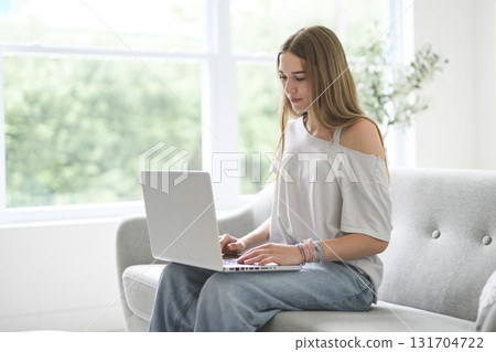Handsome teenage girl sitting at home on the couch typing on laptop 131704722