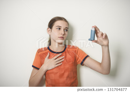 Young girl using asthma inhaler on studio white background 131704877