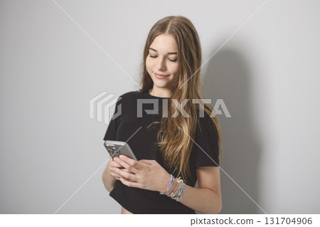 Portrait of teenage girl in casual t-shirt on light background in studio using cellphone Portrait of teenage girl in casual t-shirt on light background in studio using cellphone 131704906