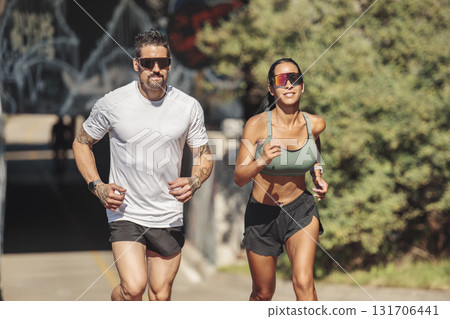 Young fitness couple running on a city on summer day Young fitness couple running on a city on summer day 131706441