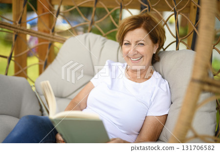 Portrait of middle aged woman reading book on hamac chair Portrait of middle aged woman reading book on hamac chair 131706582