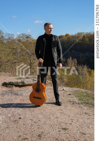 Blonde man playing string guitar outdoors in autumn forest. Concept of sound therapy, mental health and wellness rituals. Calmness tranquility audio-sensory practices. Aura farming energy Blonde man playing string guitar outdoors in autumn forest. Concept of sound therapy, mental health and wellness rituals. Calmness tranquility audio-sensory practices. Aura farming energy 131706768