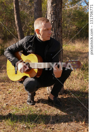Portrait of smiling caucasian artist plays wooden acoustic guitar in autumnal park. Young songwriter plays string musical instrument hobby outside in nature fall time. Audio music healing 131706771