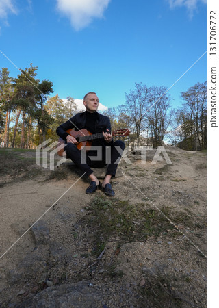 Portrait of smiling caucasian artist plays wooden acoustic guitar in autumnal park. Young songwriter plays string musical instrument hobby outside in nature fall time. Audio music healing 131706772