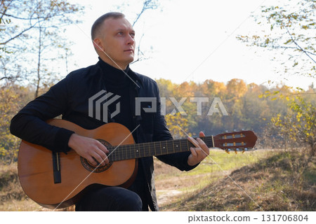 Blonde man playing string guitar outdoors in autumn forest. Concept of sound therapy, mental health and wellness rituals. Calmness tranquility audio-sensory practices. Aura farming energy Blonde man playing string guitar outdoors in autumn forest. Concept of sound therapy, mental health and wellness rituals. Calmness tranquility audio-sensory practices. Aura farming energy 131706804