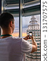 Nov 20, 2019 - Kuala Lumpur, Malaysia: Unrecognizable male adult tourist taking photo of Petronas tower with smartphone through window at colorful sunset.Observation deck visit, tourist attraction 131707575