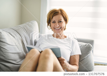 Portrait of smiling middle aged woman reading book at home Portrait of smiling middle aged woman reading book at home 131707576