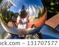 Creative reflection self-portrait of unrecognizable photographer pointing into shiny metallic sphere, blurred and distorted background of Kuala Lumpur skyline and Petronas Twin Towers. Modern 131707577