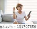 senior woman relaxing at home on the sofa reading her text messages on her mobile phone with a quiet smile 131707650