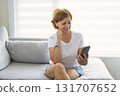senior woman relaxing at home on the sofa reading her text messages on her mobile phone with a quiet smile 131707652