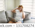 senior woman relaxing at home on the sofa reading her text messages on her mobile phone with a quiet smile 131708274