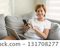 senior woman relaxing at home on the sofa reading her text messages on her mobile phone with a quiet smile 131708277