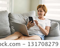 senior woman relaxing at home on the sofa reading her text messages on her mobile phone with a quiet smile 131708279