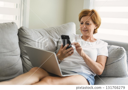 senior woman relaxing at home on the sofa reading her text messages on her mobile phone with a quiet smile senior woman relaxing at home on the sofa reading her text messages on her mobile phone with a quiet smile 131708279