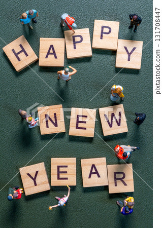 Miniature figurines surrounding wooden letter tiles forming the phrase Happy New Year 131708447