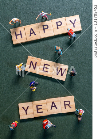 Miniature figurines surrounding wooden letter tiles forming the phrase Happy New Year 131708452