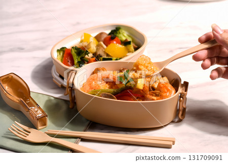A colorful paella and steamed vegetable lunch packed in a beige lunch box 131709091
