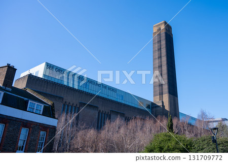 Visitors enjoy a clear day outside Tate Modern, a prominent art museum in London. The striking architecture and surrounding greenery provide a beautiful backdrop for art lovers. Visitors enjoy a clear day outside Tate Modern, a prominent art museum in London. The striking architecture and surrounding greenery provide a beautiful backdrop for art lovers. 131709772