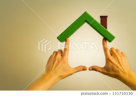 Hands forming a house shape with green roof on neutral background symbolizing home ownership real estate and eco living 131710130