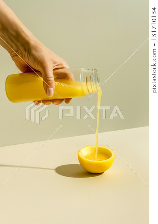Hand pouring citrus juice from glass bottle into lemon half on neutral background Hand pouring citrus juice from glass bottle into lemon half on neutral background 131710134
