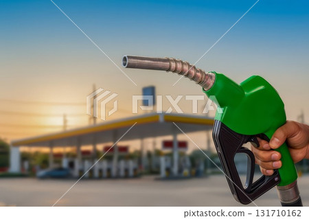 Green gas pump nozzle in hand with fuel station blurred at sunset 131710162