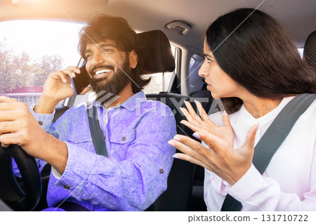 Frustrated Indian woman gesturing while man talks on phone while driving Frustrated Indian woman gesturing while man talks on phone while driving 131710722