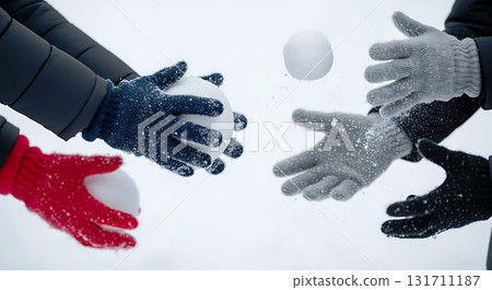 Four gloved hands in different colored gloves are tossing and catching snowballs mid-air, creating a dynamic winter scene. The background is blurred to highlight the action 131711187
