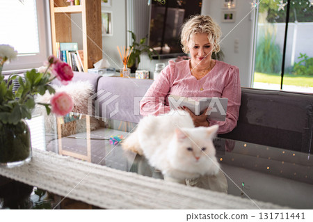 Adult woman reading book at home with pet cat 131711441