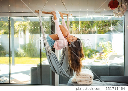 Girl playing upside down in indoor swing at home Girl playing upside down in indoor swing at home 131711464
