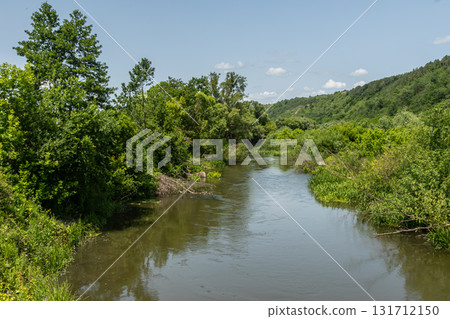 Serene river winding through lush greenery under a clear sky during daytime at a rural landscape 131712150