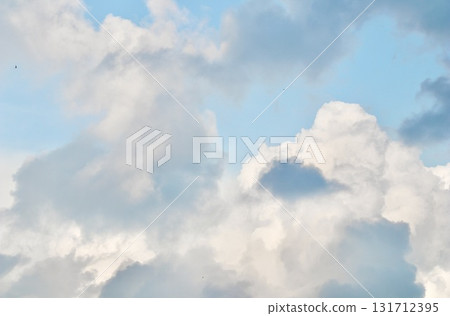 A mix of dark grey storm clouds and bright white cumulus formations against a pale blue sky, showing the transition of weather and dramatic atmospheric contrast. 131712395