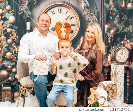 Smiling family posing together in cozy Christmas setting with gifts, tree, and warm lights. Joyful atmosphere and classic studio style Smiling family posing together in cozy Christmas setting with gifts, tree, and warm lights. Joyful atmosphere and classic studio style 131712702
