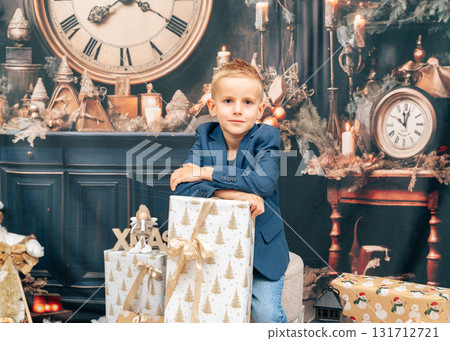 Wide composition shows a boy leaning against stacked gifts in front of an ornate mantel and clock. Natural, commercial-friendly holiday shot for catalogs and family ads Wide composition shows a boy leaning against stacked gifts in front of an ornate mantel and clock. Natural, commercial-friendly holiday shot for catalogs and family ads 131712721