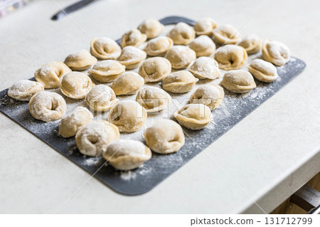 Raw homemade dumplings arranged on a floured board in the kitchen. Traditional cooking process before boiling. Close-up of uncooked pelmeni 131712799